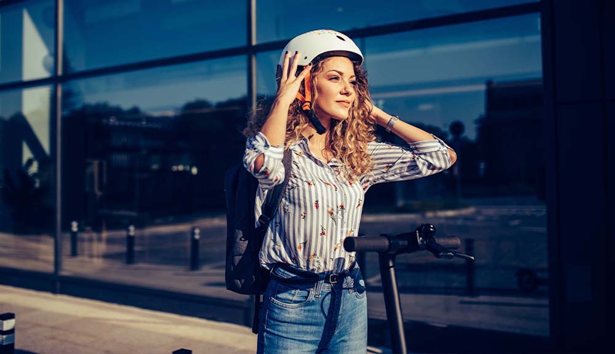 A woman wearing a helmet is standing next to a scooter.