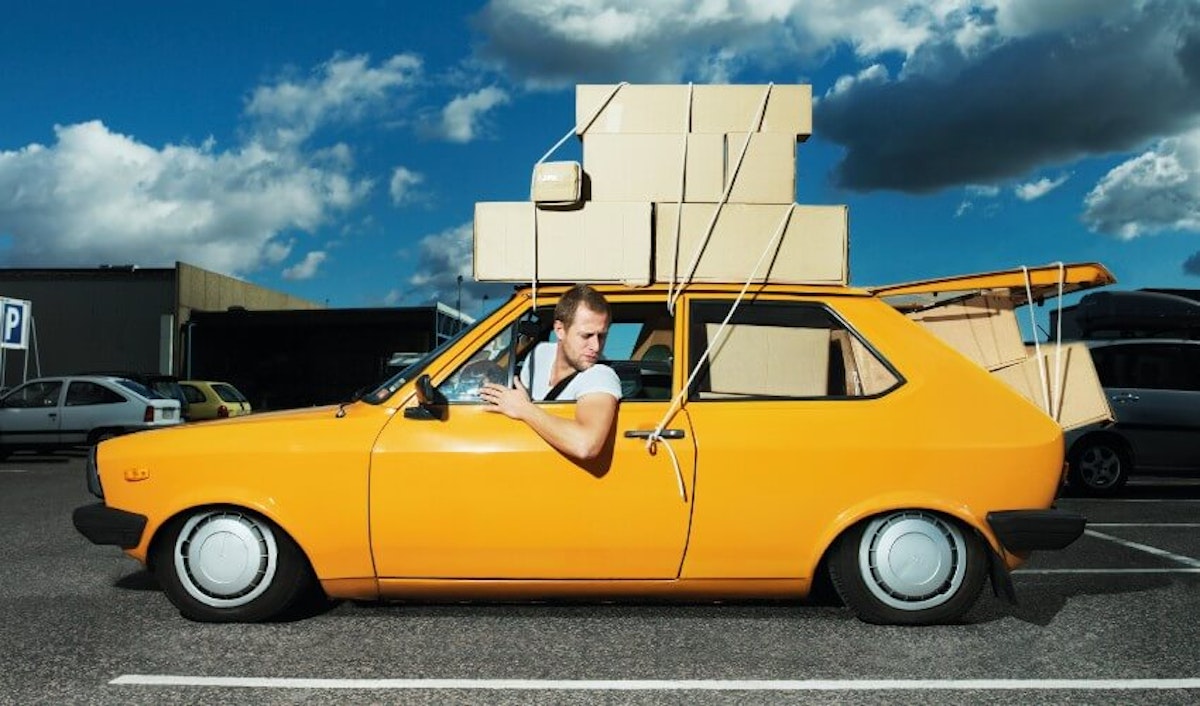 A man in a yellow car with boxes on top.