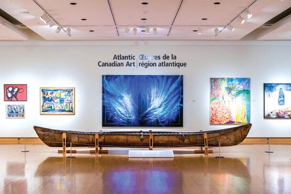 An exhibition of atlantic canadian art featuring colorful paintings and a traditional canoe displayed in a gallery.