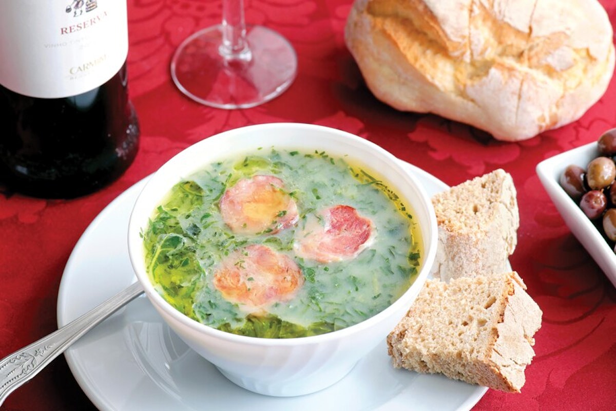 A bowl of soup with bread and wine on a table.