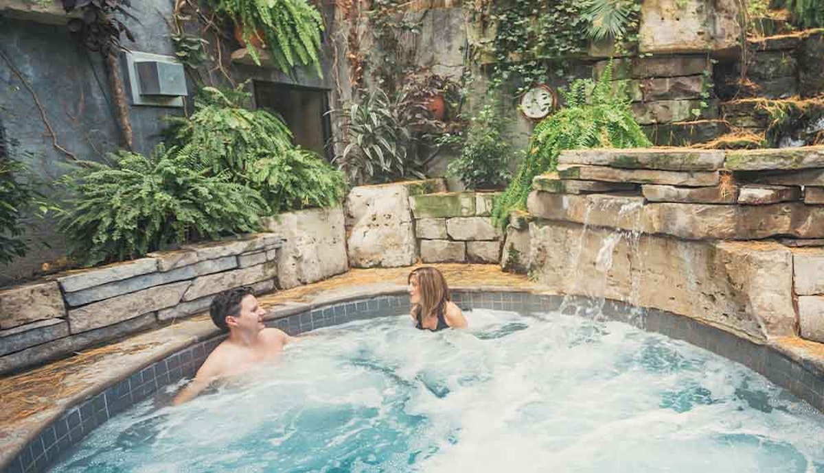 A man and woman relaxing in a hot tub in a garden.