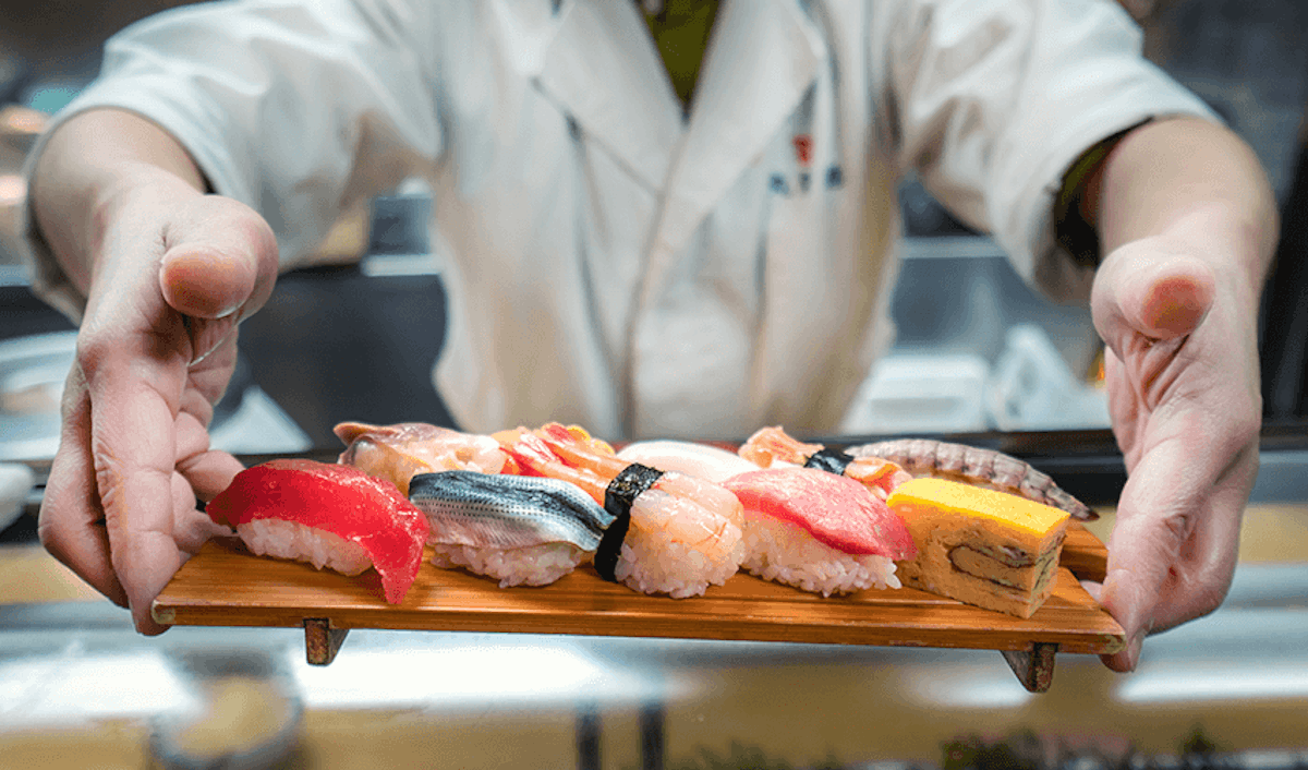 A sushi chef holding a tray of sushi.