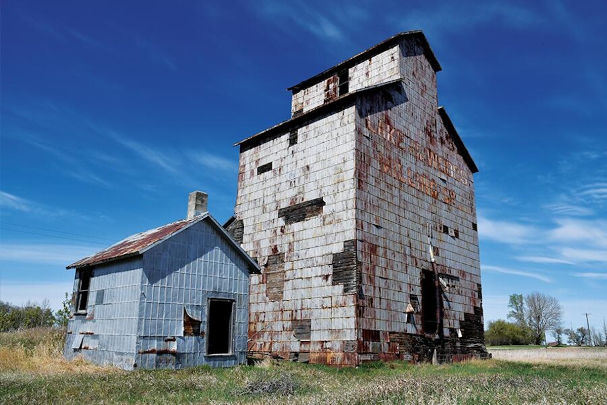 An old grain elevator sits in the middle of a field.