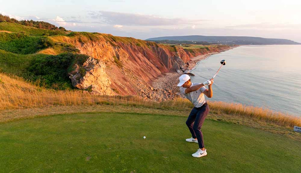 A woman is playing golf on a cliff overlooking the ocean.