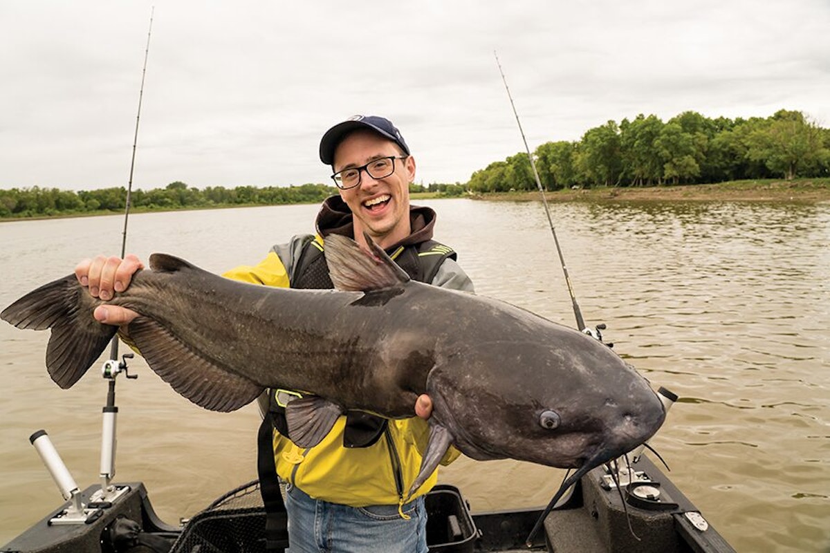 A man holding up a catfish in a boat.