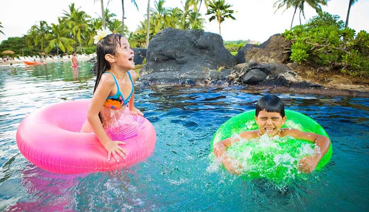 Two children playing in a pool with inflatable rafts.