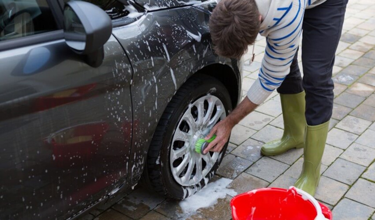 A man washing his car's tire with a bucket of soap.