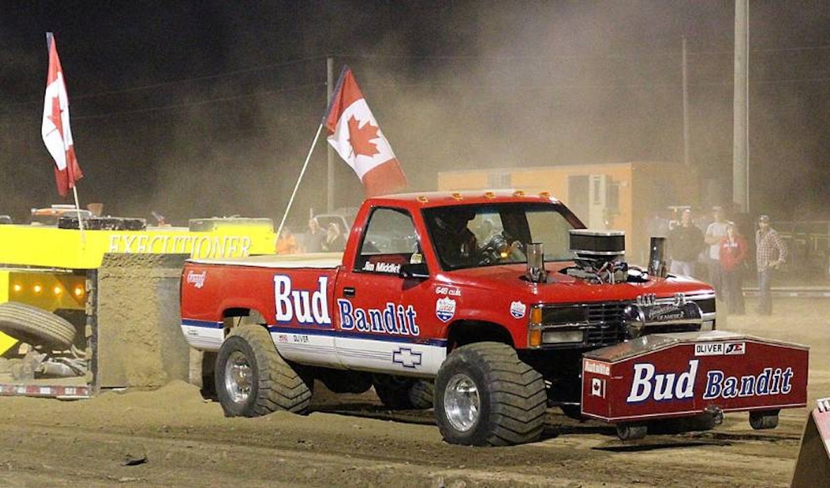 A red truck with a canadian flag on it driving down a dirt track.
