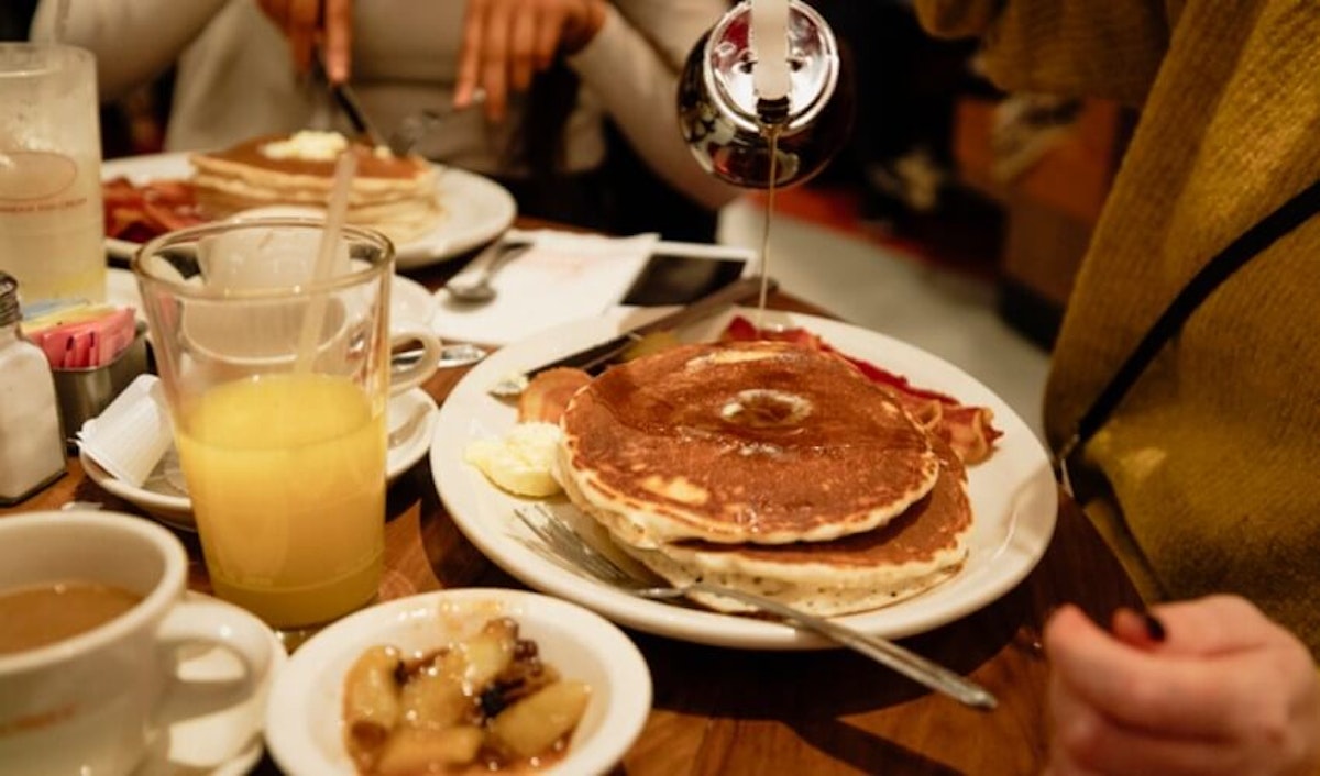A person is pouring syrup on a plate of pancakes.