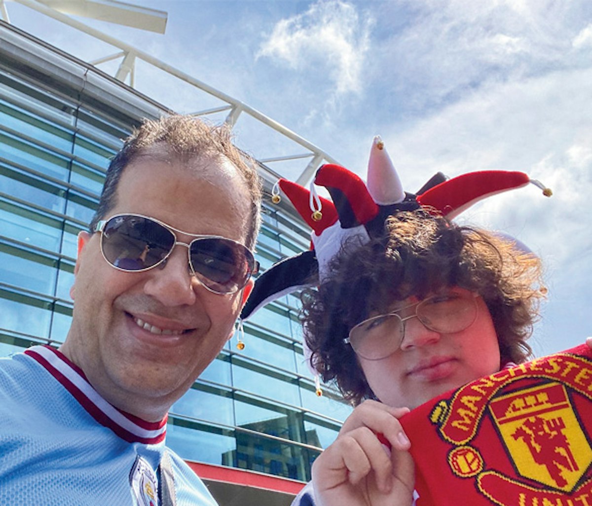 Two soccer fans posing for a selfie, one wearing a jester hat and holding a manchester united scarf.