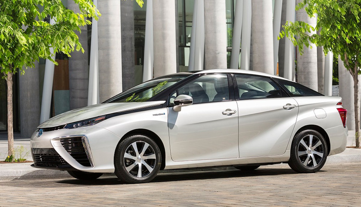 A white toyota mirai fuel cell vehicle parked on a city street.