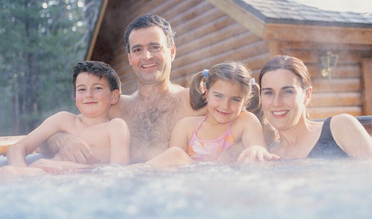 A family in a hot tub in front of a cabin.