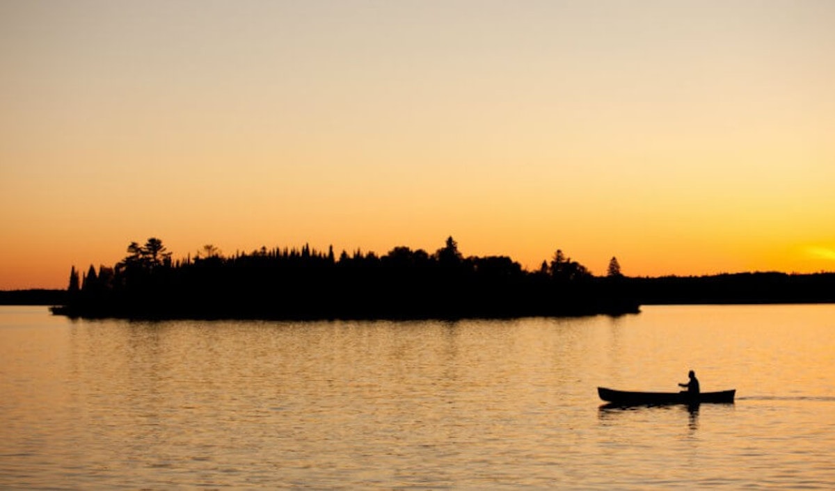 A man in a canoe on a lake at sunset.