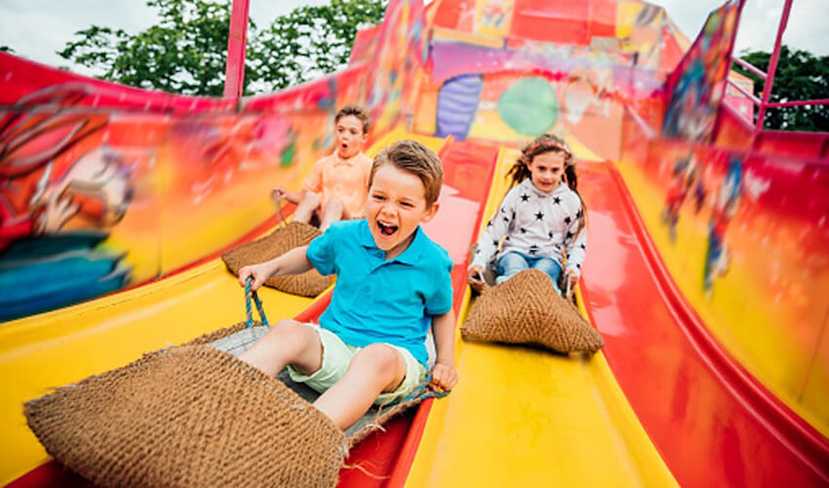 A group of children riding down a slide at an amusement park.