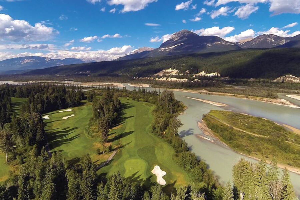 An aerial view of a scenic golf course with a river winding through the mountains in the background.
