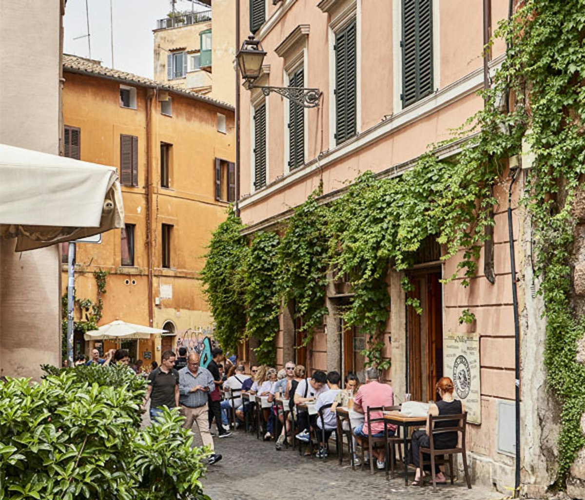 People are sitting at tables in a narrow alley in rome, italy.