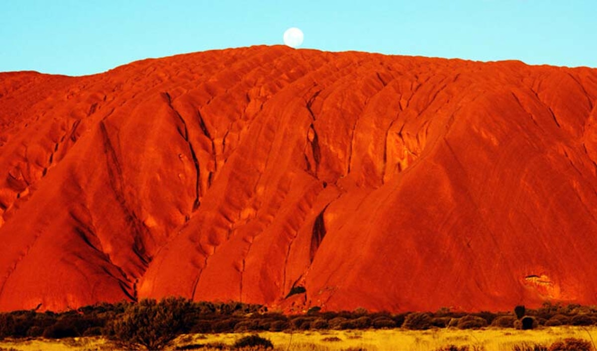 The moon rises over uluru in the australian outback.