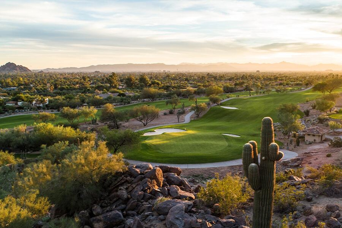 A scenic golf course at sunset with cacti and rugged terrain in the foreground.