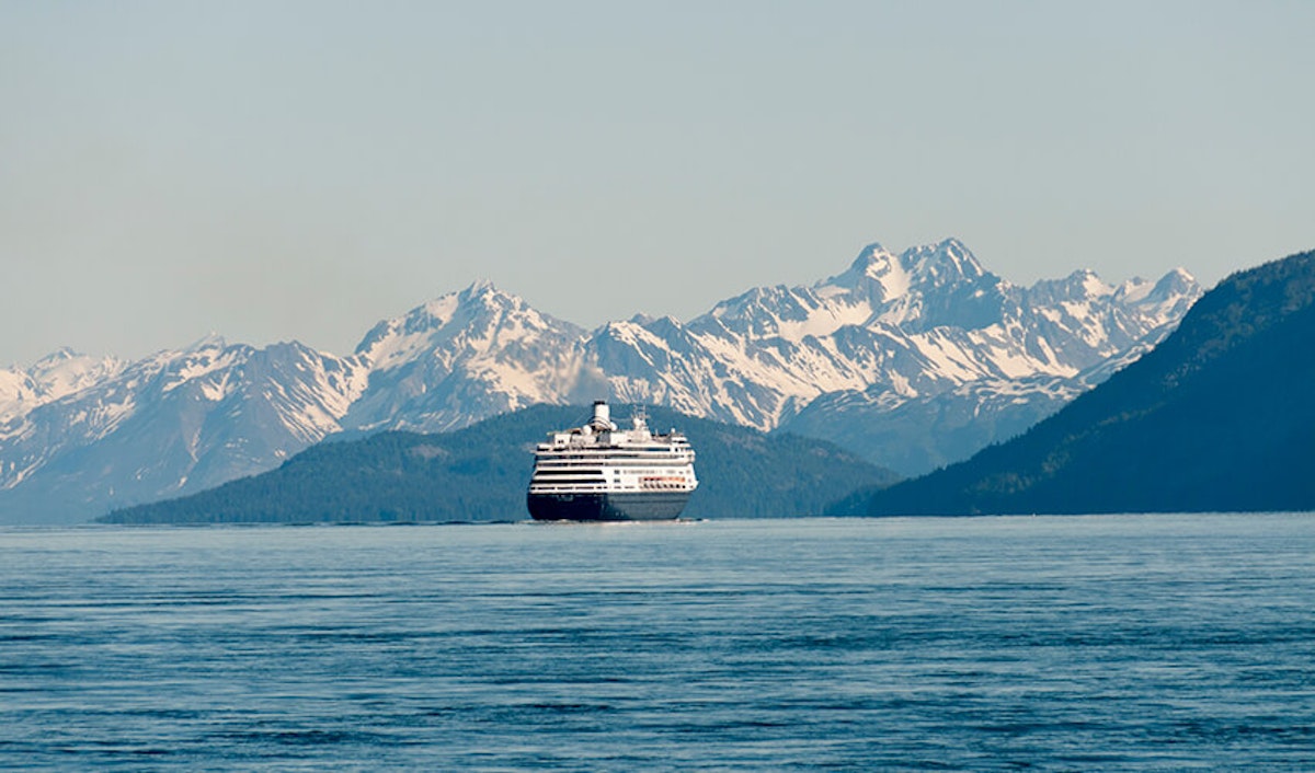 Cruise ship sailing in front of a mountain range.