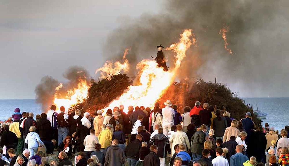 A crowd of people watching a bonfire on the beach.