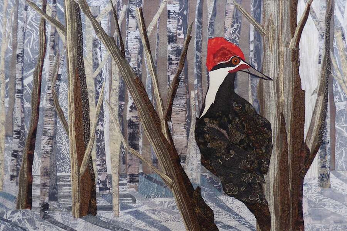 A textile art depiction of a woodpecker among stylized trees.
