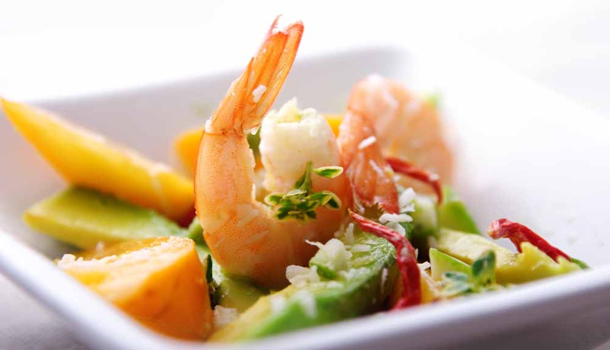 A white bowl with shrimp, avocado, and peaches.