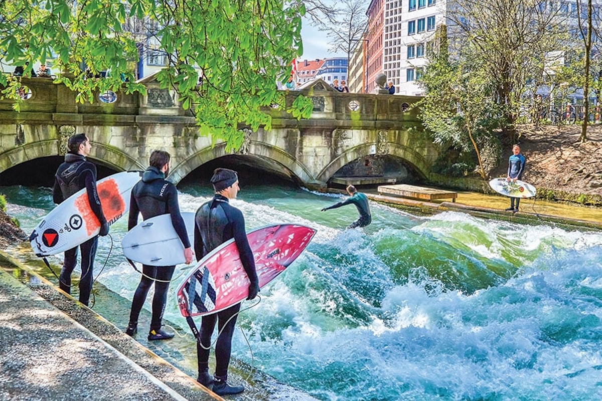 A group of surfers standing next to a river with surfboards.