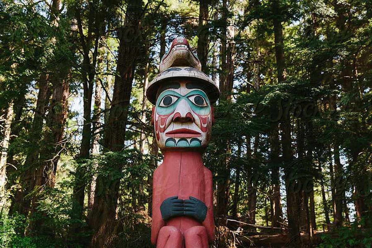A totem pole stands in the middle of a forest.