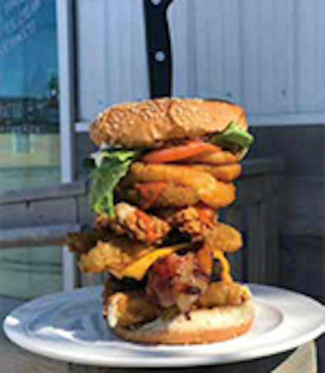 A towering multi-layered burger with various fillings and a knife stabbed through the center for support.