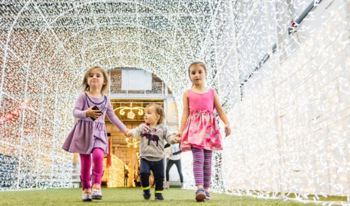 Three children walking through a tunnel of lights.