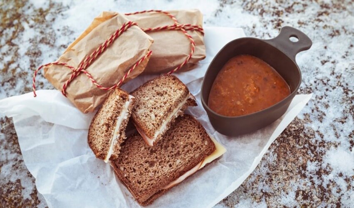 A sandwich with tomato sauce and a cup of soup.