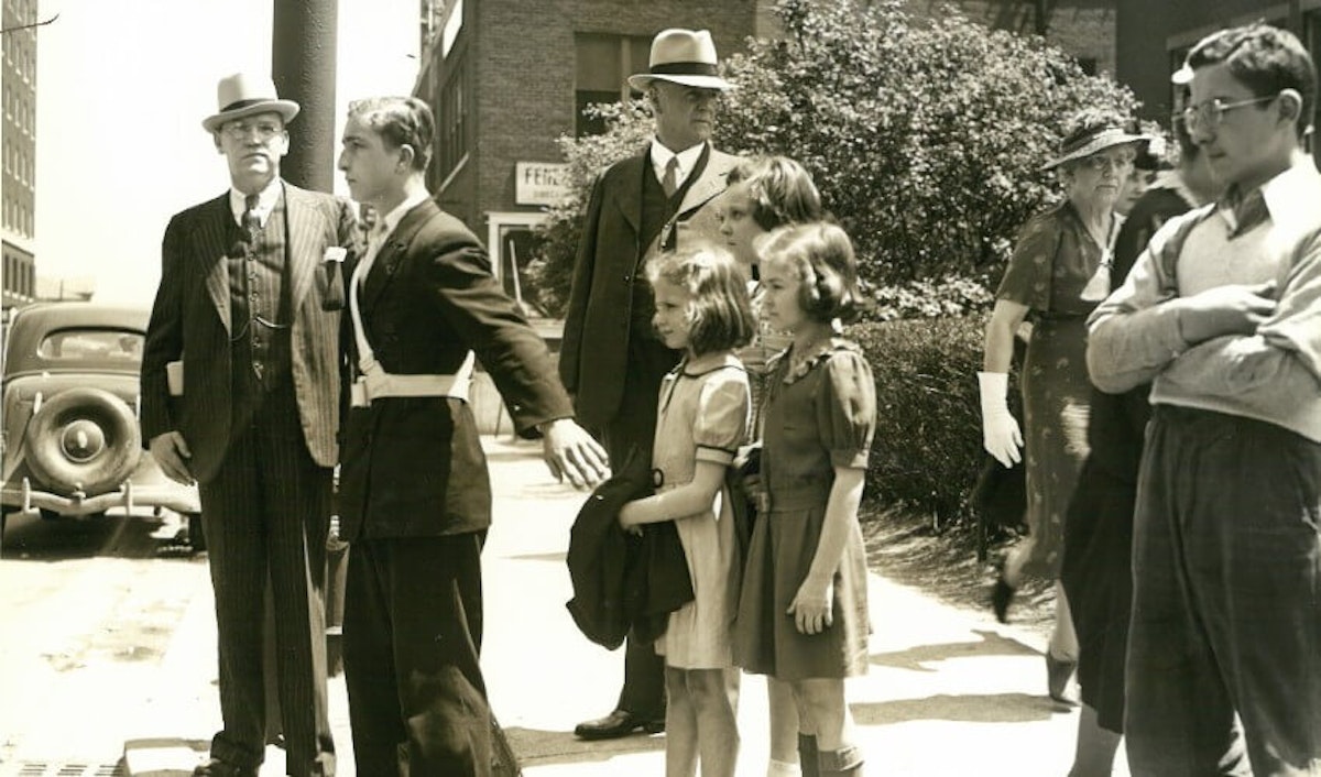 An old photo of a group of people standing on a sidewalk.
