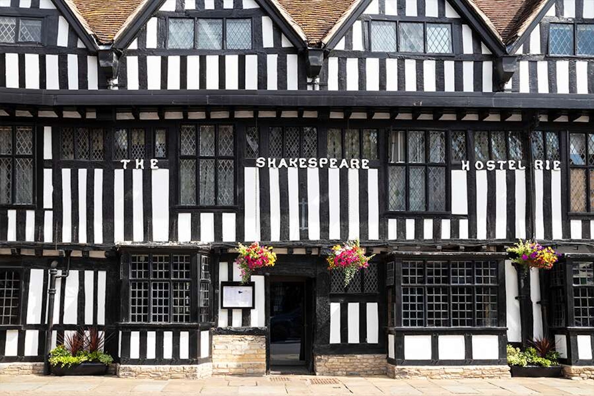 Black and white tudor-style building with "the shakespeare hostelrie" sign and hanging flower baskets.