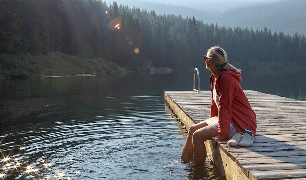 A person sitting on a wooden dock by a serene lake, surrounded by forest, enjoying a tranquil moment in nature.