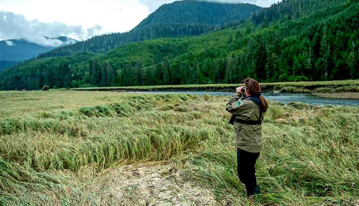 A woman is standing in a grassy field near a river.