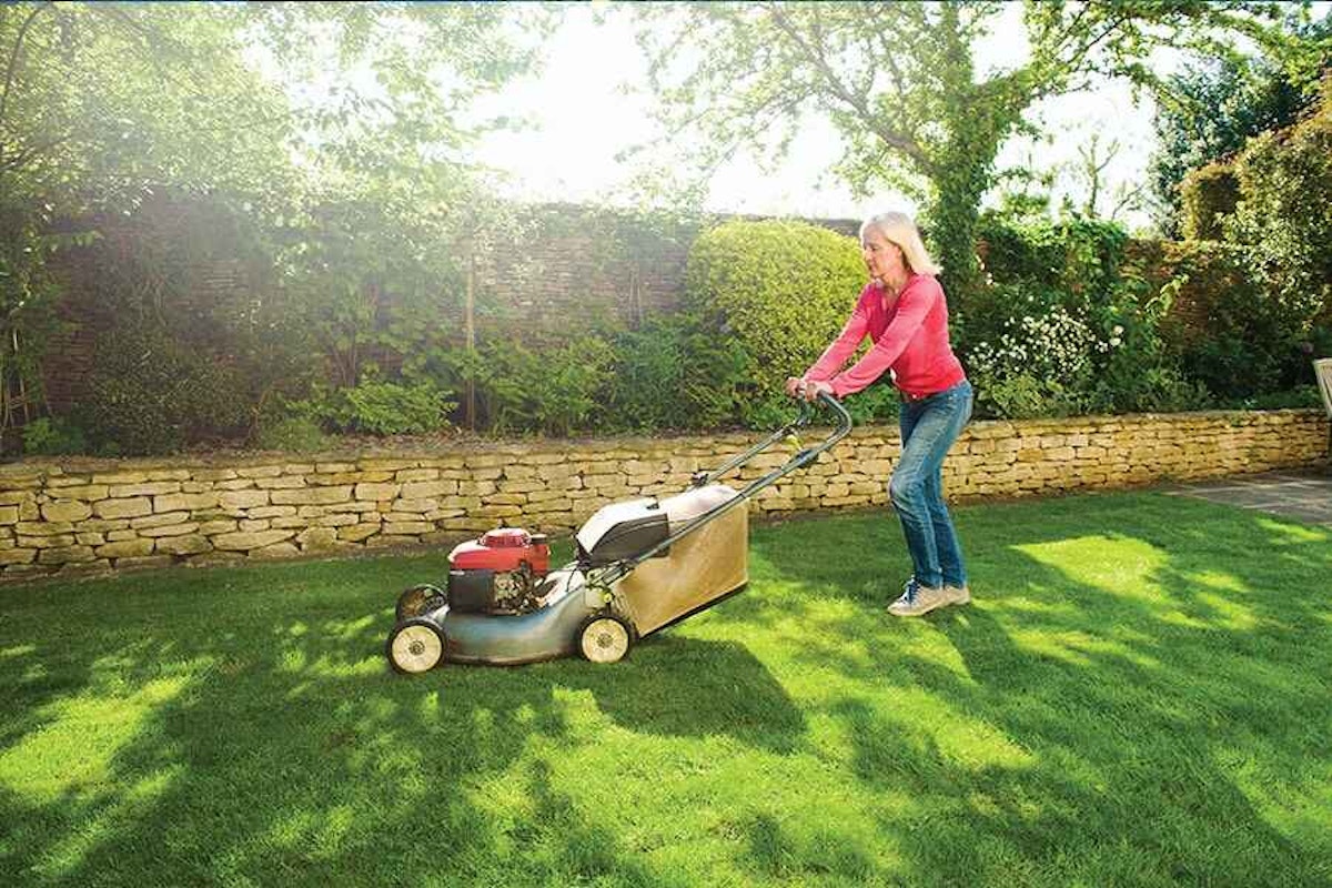 A woman is mowing her lawn with a lawn mower.