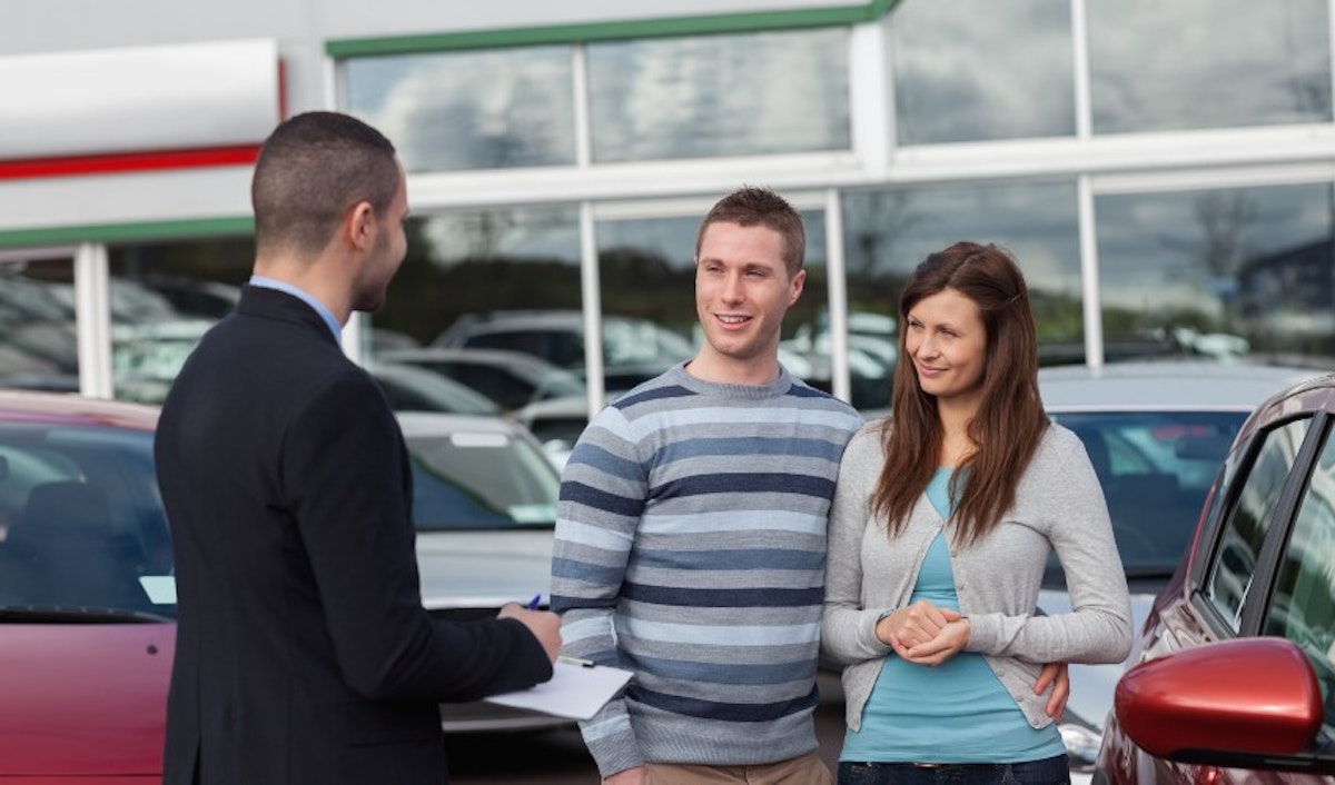 A man and woman standing in front of a car dealership.