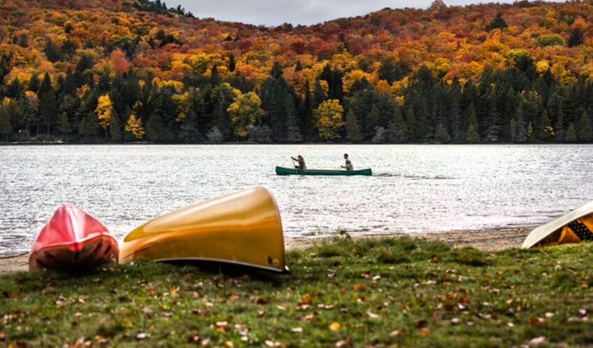 Canoes on the shore of a lake with trees in the background.