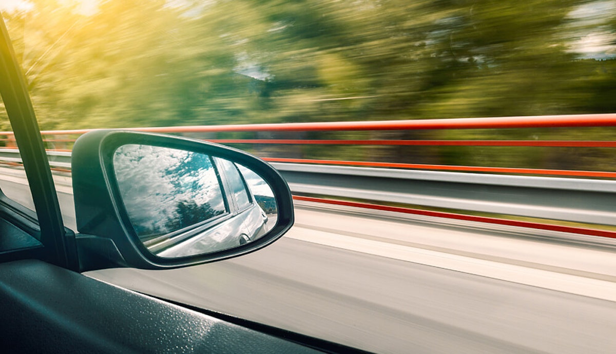 View of a car's side mirror on a highway, reflecting the scenery, with motion blur suggesting high speed.