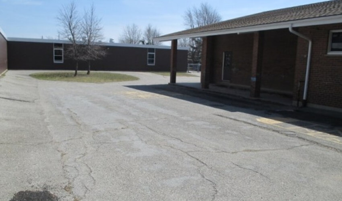 Empty school parking lot with cracked pavement and a covered walkway on a sunny day.