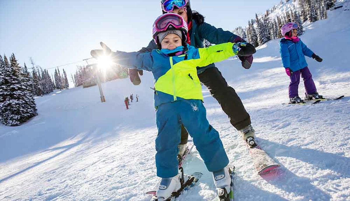A woman with a child on skis on a snowy slope.