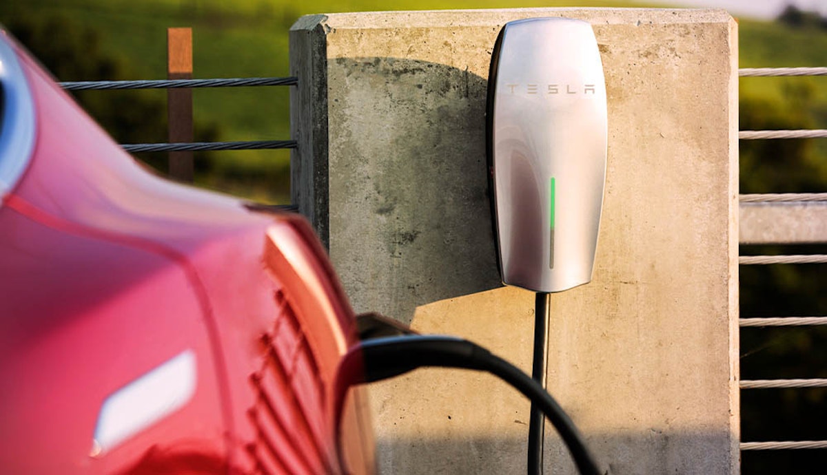 A red tesla car is plugged into an electric charger.