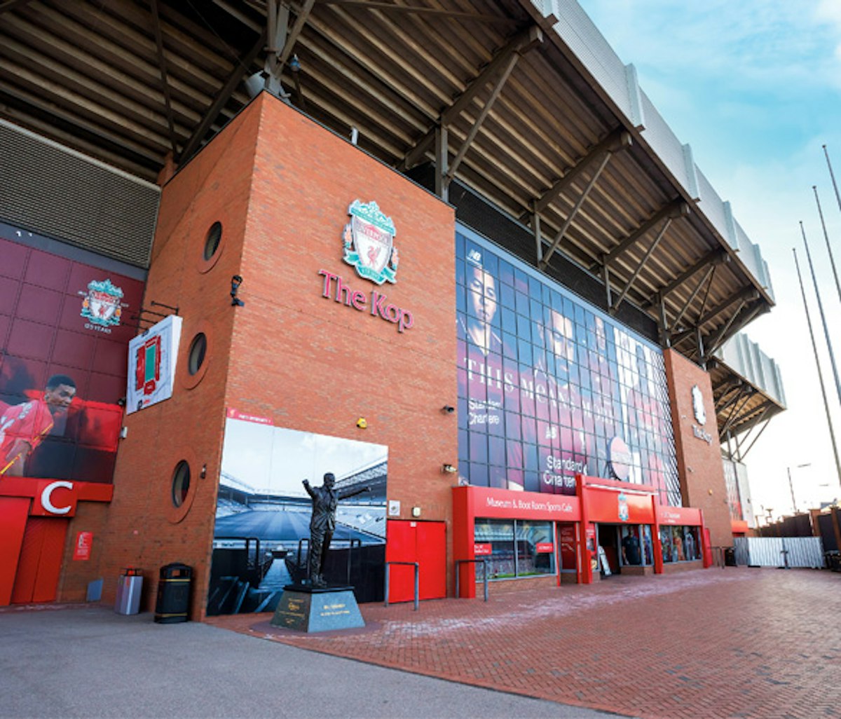 Exterior view of the kop entrance at anfield stadium with a statue and commemorative plaques.