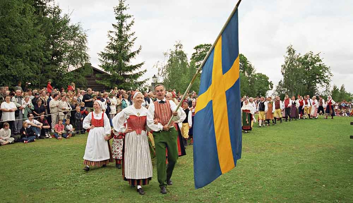 A group of people dressed in traditional swedish clothing holding a swedish flag.