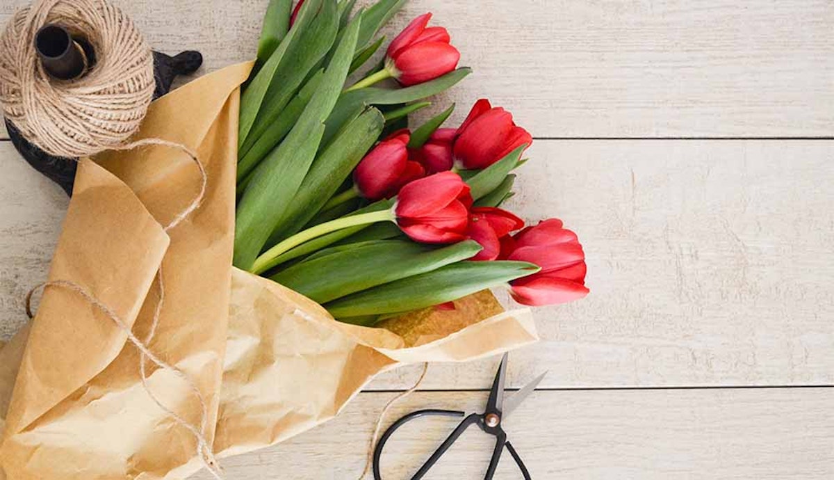 A bouquet of red tulips and scissors on a wooden table.