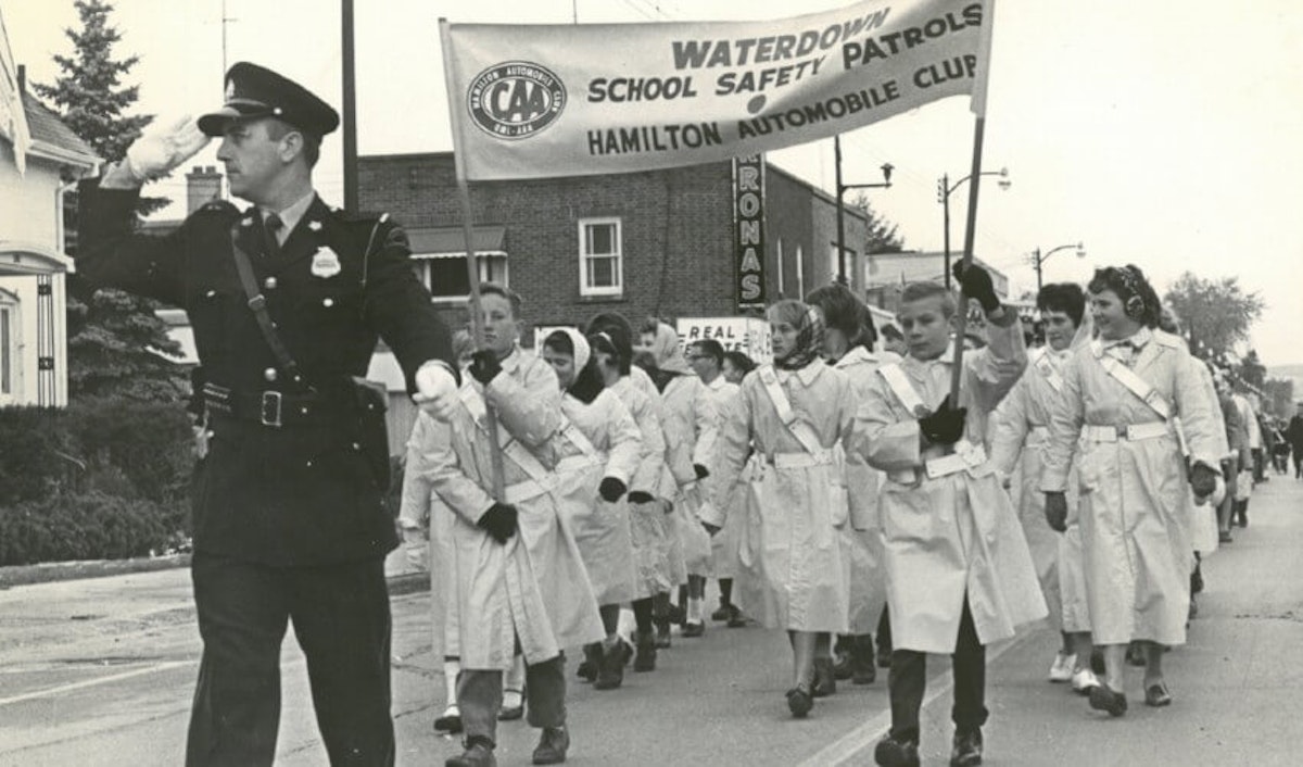 A group of children in white uniforms marching down a street.
