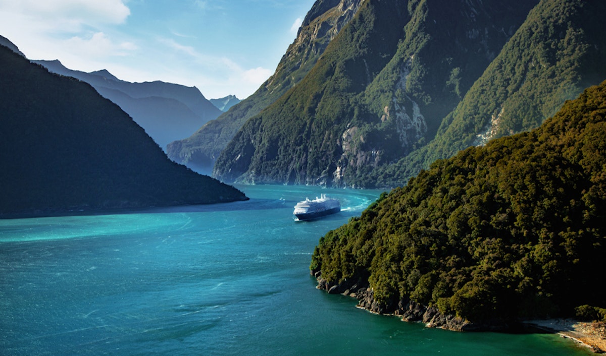 A cruise ship is traveling down a river near mountains.