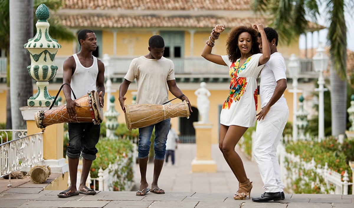 A group of people playing drums in front of a mansion.