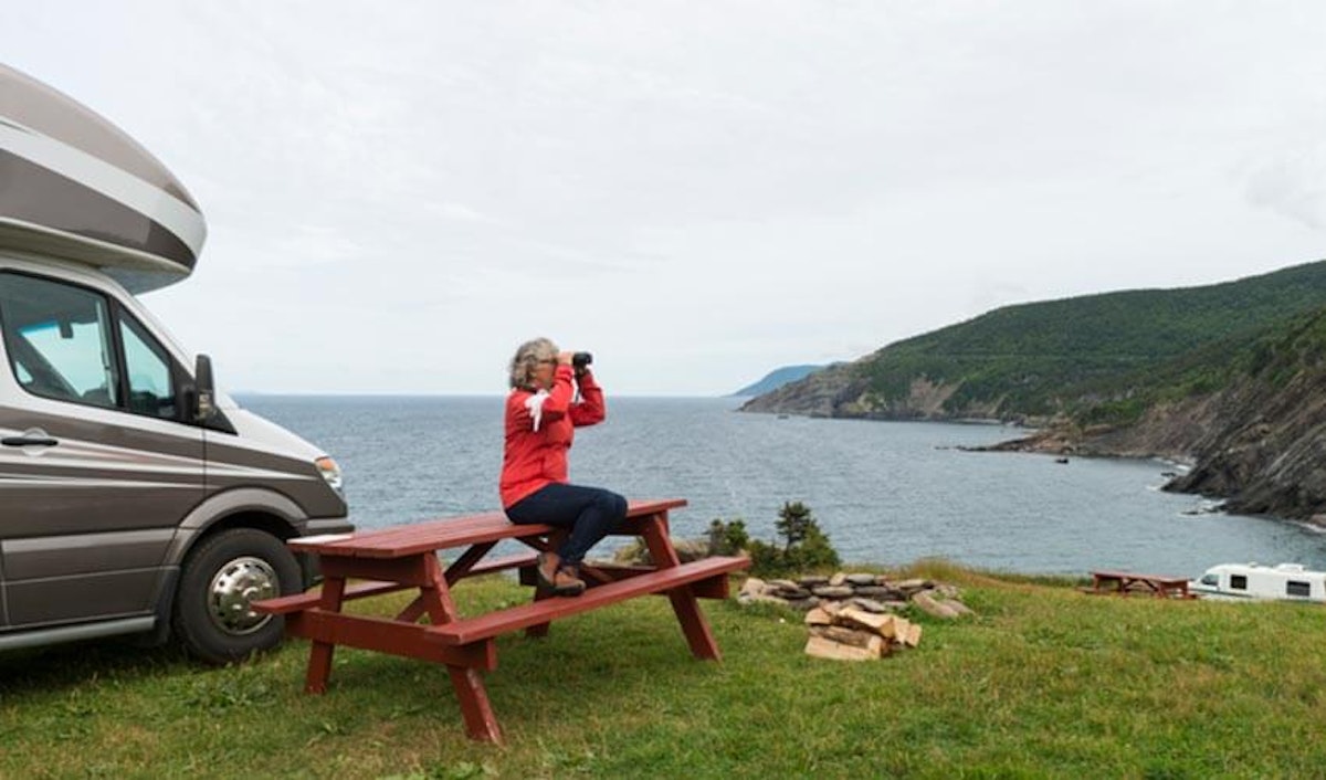 A woman sits at a picnic table in front of an rv.