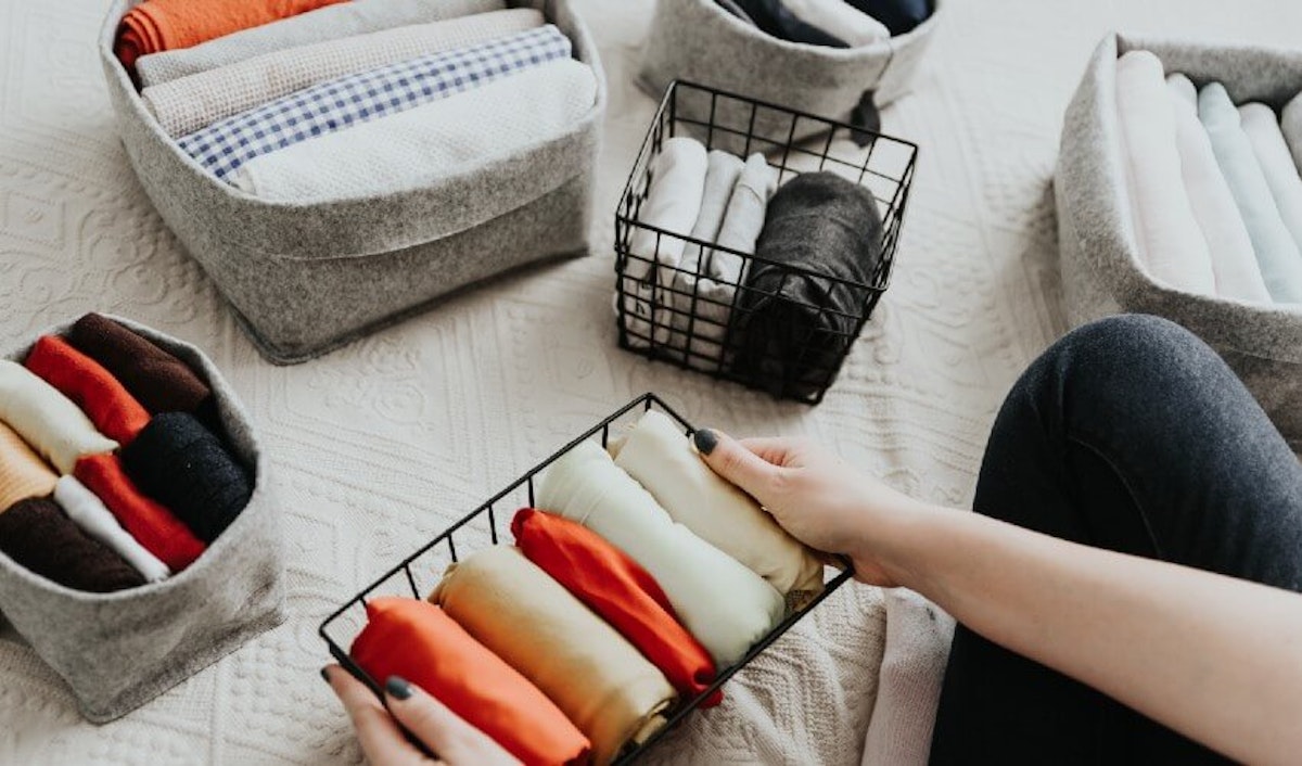 A woman is putting clothes into baskets on a bed.